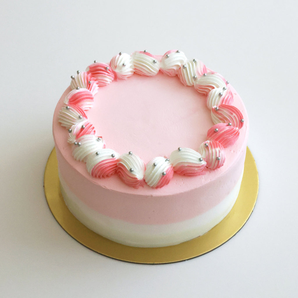 Pink and white cake with decorative edge on a gold plate against a white background