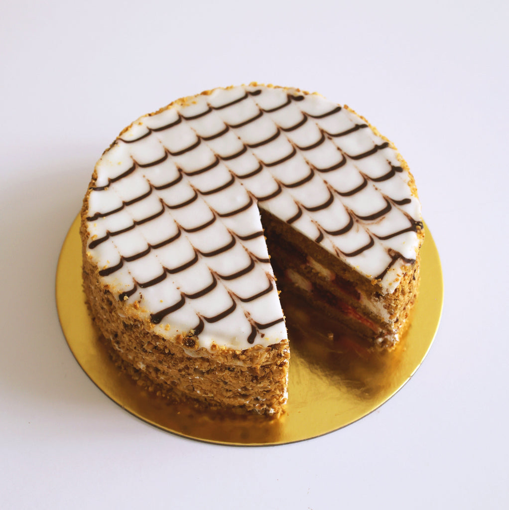 Round cake with white frosting on a gold cake stand against a white background